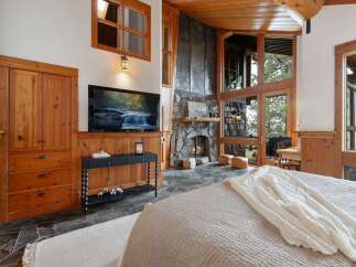 Experience rustic luxury in this stunning bedroom featuring a grand stone fireplace and expansive windows that bring the outdoors in.