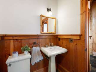 This charming bathroom features rustic wood paneling and a classic pedestal sink, creating a warm and inviting atmosphere.