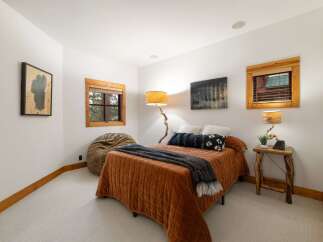 This cozy bedroom features a warm, rust-colored quilted bedspread, complemented by dark accent pillows and a plush throw blanket.