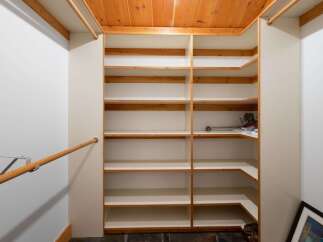 Discover ample storage solutions in this spacious walk-in closet, featuring a custom-built shelving system with multiple levels and a convenient wooden handrail.