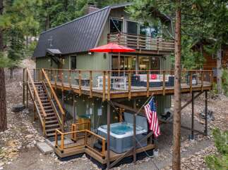 Experience mountain living in this charming cabin featuring a spacious deck with a hot tub and an American flag.