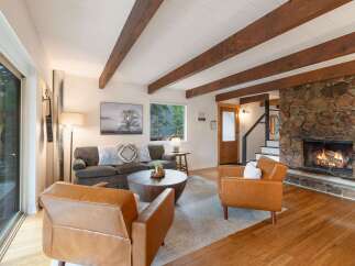 Experience cozy living in this inviting living room, featuring a striking stone fireplace and warm wooden beams overhead.