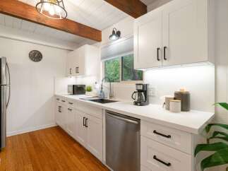 This charming kitchen boasts modern white cabinetry and sleek black hardware, complemented by a durable quartz countertop.
