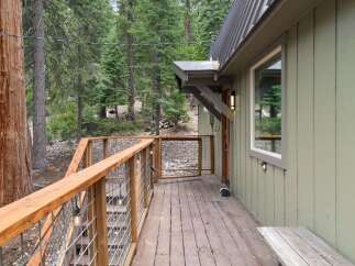 Experience the charm of this mountain retreat, featuring a spacious wooden deck with a rustic metal railing, perfect for enjoying the surrounding pine forest.