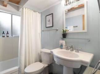 This charming bathroom features a clean white pedestal sink with modern chrome fixtures, complemented by a large mirror and a decorative framed picture on the light blue paneled wall.