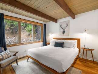 Experience serene living in this charming bedroom, featuring a large window with forest views and a cozy, inviting bed.