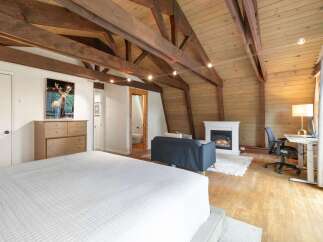 Experience rustic charm in this unique attic bedroom, featuring exposed wooden beams and a cozy fireplace.