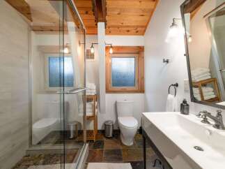 Experience rustic charm in this beautifully appointed bathroom, featuring a spacious glass-enclosed shower with pebble flooring and elegant wood accents.