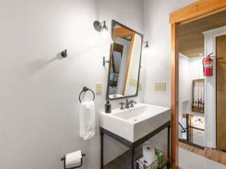 This charming bathroom features a stylish vessel sink atop a dark metal vanity, complemented by a rustic framed mirror and industrial-style sconces.