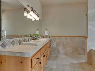 This spacious bathroom features a double vanity with a stone countertop and a decorative tile backsplash.