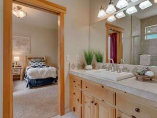 This charming bathroom features a spacious vanity with ample storage and a clean white sink, complemented by a large mirror reflecting the adjacent bedroom.