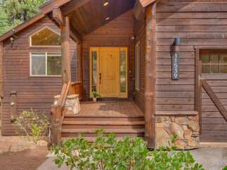 Experience rustic charm with this beautiful wooden cabin featuring a welcoming porch and a bright yellow front door.
