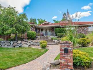 Discover this charming brick home featuring a welcoming pathway leading to the entrance, surrounded by lush greenery and mature trees.