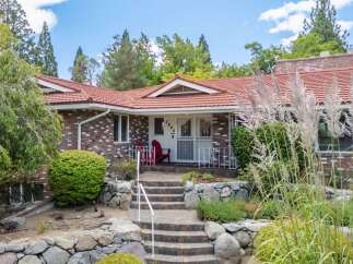 Charming brick home with a red tile roof, offering a welcoming entrance with stone landscaping and a paved walkway leading to the front door.
