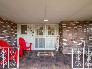 Welcome guests to this charming home with a festive front porch, featuring two bright red Adirondack chairs perfect for relaxing.