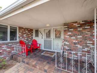 Welcome guests to this charming home with a welcoming front porch featuring two bright red Adirondack chairs.