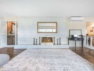 This spacious living room features a stunning white brick fireplace as the focal point, complemented by a large ornate mirror and a modern gas fireplace.