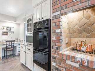 This kitchen features a built-in double oven and a charming brick fireplace with a grill.