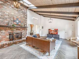 Experience modern living in this stunning living room featuring a dramatic vaulted ceiling with exposed beams and a cozy brick fireplace.