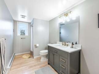 This modern bathroom features a stylish gray vanity with gold hardware, complemented by a white quartz countertop and a sleek undermount sink.