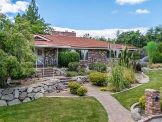 Discover this charming brick home featuring a welcoming red tile roof and lush landscaping.
