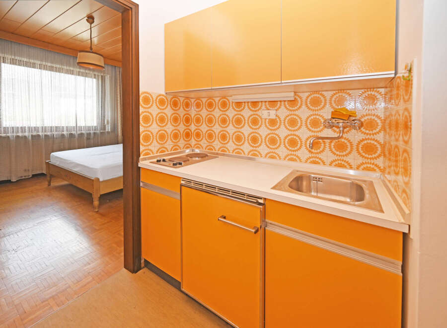 Discover this charming studio apartment featuring a functional kitchenette with vibrant orange cabinetry and a retro-inspired tiled backsplash.