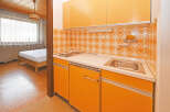 Discover this charming studio apartment featuring a functional kitchenette with vibrant orange cabinetry and a retro-inspired tiled backsplash.