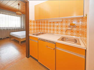 Discover this charming studio apartment featuring a functional kitchenette with vibrant orange cabinetry and a retro-inspired tiled backsplash.