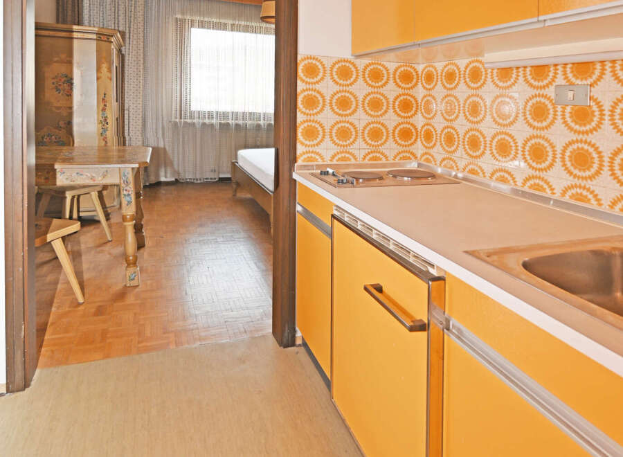 Step into a charming retro kitchen featuring vibrant orange cabinetry and a unique sunburst tile backsplash.