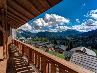 Experience breathtaking mountain views from this charming wooden balcony, overlooking a picturesque village nestled in the Alps.