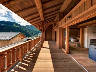 Experience the charm of mountain living with this stunning wooden balcony offering breathtaking views of lush green hills and a clear blue sky.