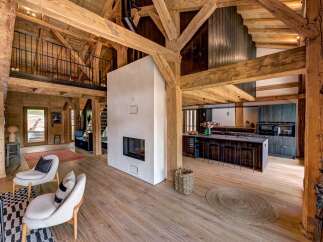 Experience rustic luxury in this stunning timber-framed home, featuring an open-concept living space with a modern fireplace and a sleek, dark wood kitchen island.