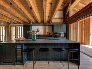 Experience luxury mountain living in this stunning kitchen featuring a spacious dark wood island with a built-in wine cooler and modern bar stools.
