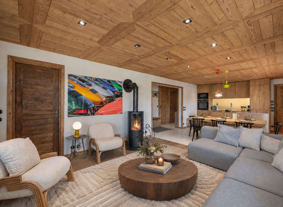 Experience luxury mountain living in this stunning chalet, featuring a warm and inviting living area with a modern wood-burning fireplace and a striking art piece.