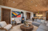 Experience luxury mountain living in this stunning chalet, featuring a warm and inviting living area with a modern wood-burning fireplace and a striking art piece.