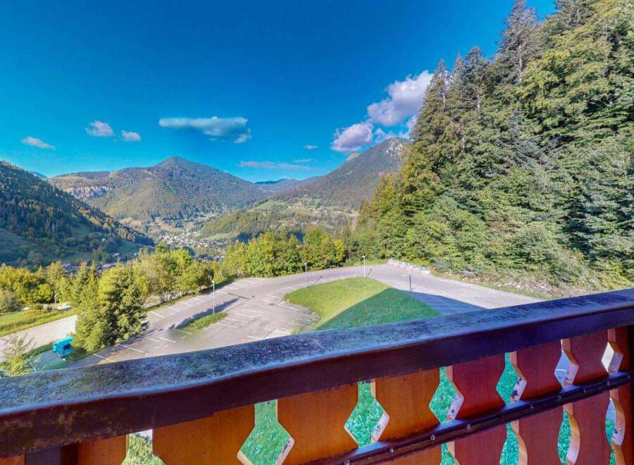 Experience breathtaking mountain views from this property, featuring a spacious balcony overlooking a scenic valley and surrounding evergreen forests.