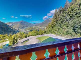 Experience breathtaking mountain views from this property, featuring a spacious balcony overlooking a scenic valley and surrounding evergreen forests.