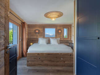 Experience rustic luxury in this charming bedroom, featuring a cozy wooden bed frame and stunning mountain views through the windows.