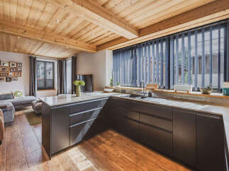 Experience modern alpine living in this stunning kitchen and living area, featuring a sleek, dark-toned kitchen island with ample counter space and integrated drawers.