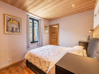 This charming bedroom features a cozy bed with a floral duvet, complemented by a wooden ceiling and walls that add a rustic touch.