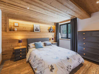 Experience rustic charm in this cozy bedroom, featuring warm wooden walls and ceiling, complemented by a comfortable bed with a floral duvet.