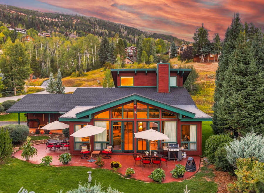 Experience luxury mountain living in this stunning home, featuring expansive windows that showcase breathtaking sunset views and a vibrant sky.