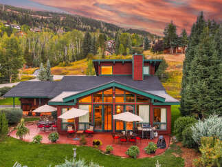 Experience luxury mountain living in this stunning home, featuring expansive windows that showcase breathtaking sunset views and a vibrant sky.