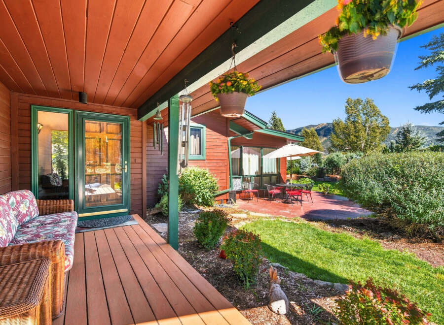 Enjoy the serene mountain views from this charming cabin's covered porch, complete with a cozy wicker sofa and hanging flower baskets.