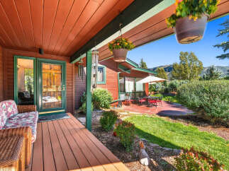 Enjoy the serene mountain views from this charming cabin's covered porch, complete with a cozy wicker sofa and hanging flower baskets.