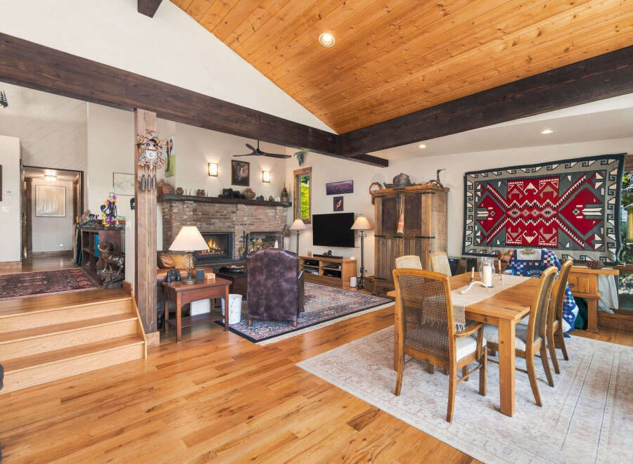 Experience rustic charm in this spacious living and dining area, featuring a grand brick fireplace and exposed wooden beams.