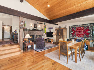 Experience rustic charm in this spacious living and dining area, featuring a grand brick fireplace and exposed wooden beams.
