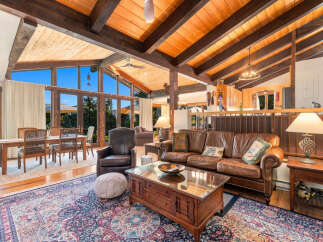 Experience rustic charm in this spacious living area, featuring a vaulted wood-beamed ceiling and expansive windows that flood the space with natural light.