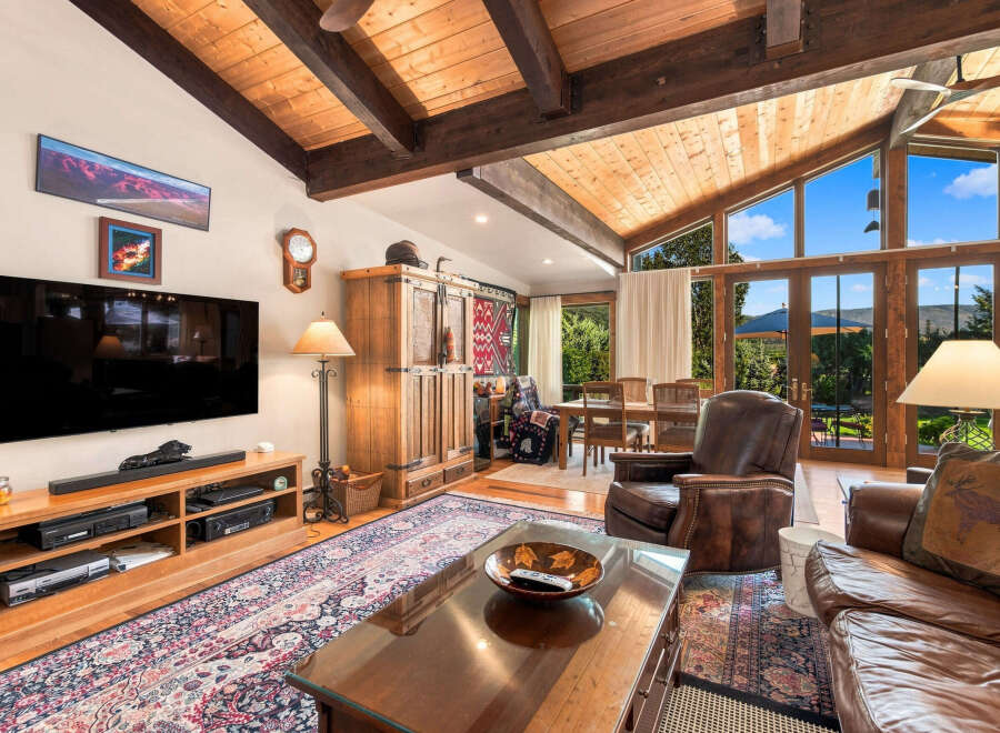 Experience rustic charm and breathtaking views in this spacious living area, featuring a vaulted wood-beamed ceiling and expansive windows that flood the room with natural light.