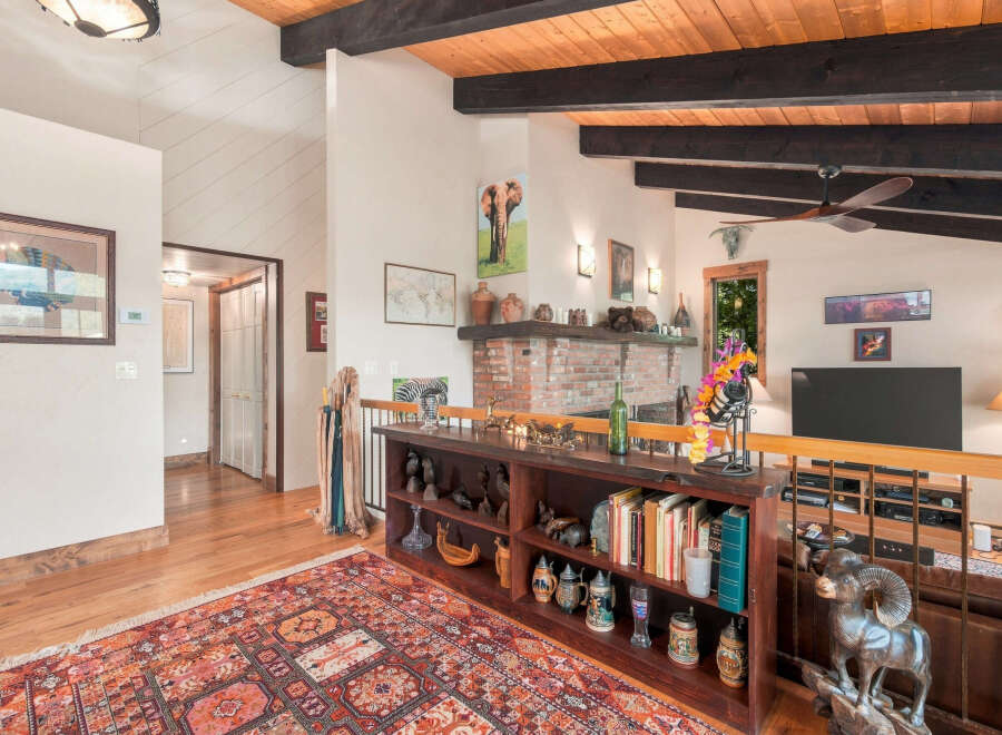 Experience rustic charm in this spacious living area featuring a vaulted wood-beamed ceiling and a cozy brick fireplace.
